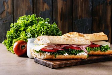 Bagetel smos met hesp en tomaat op houten plank